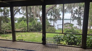 Quarto com grandes janelas voltadas para um lago, um tapete estampado e uma estante de metal.