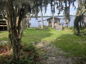 Ein Haus am See mit einem grasbewachsenen Garten, einer hölzernen Anlegestelle und einem Baum mit hängenden Moos.
