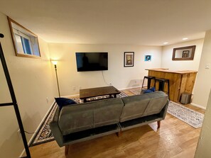 Een woonkamer met een bank, een televisie, een houten bar en een kleine tafel.