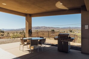 Une terrasse extérieure avec une table et des chaises, un barbecue et une vue sur un paysage désertique.