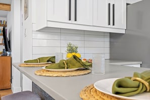 A kitchen with white cabinets, a tiled backsplash, and a countertop with plates, napkins, and a glass.