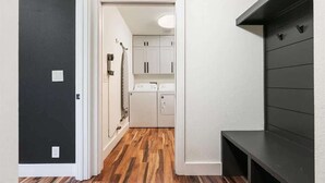 Un passadís amb una porta fosca, una zona de bugaderia amb una rentadora i un moble prestatge negre.
