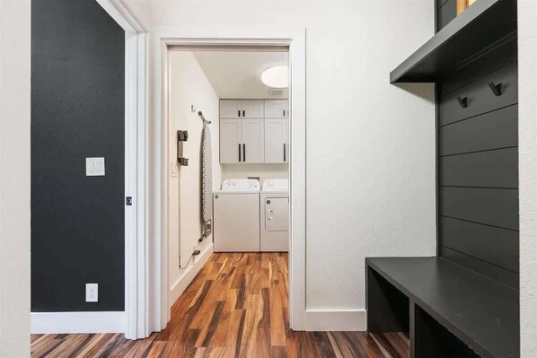 A hallway with a dark door, a laundry area with a washing machine, and a black shelf unit. - Casa Verde! Mid Century Charmer in Old Town. Walk to SWU and The Square! (Georgetown)