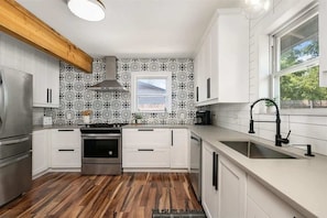 A modern kitchen with white cabinets, a stainless steel refrigerator, a built-in oven, and a window with a view.