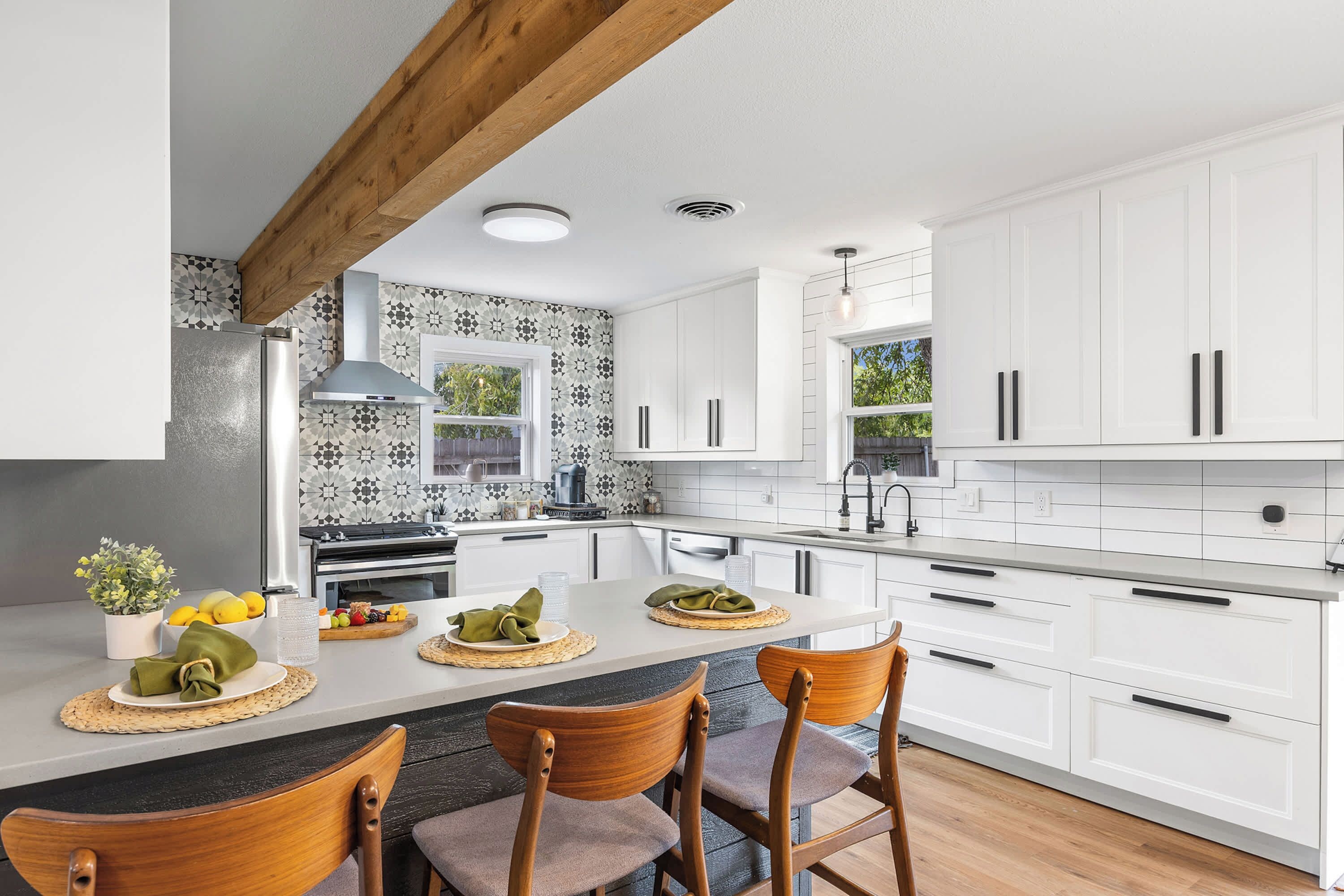 A modern kitchen with white cabinetry, a central island with seating, and a patterned backsplash.