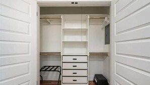 Ein begehbarer Kleiderschrank mit offenen Türen, ausgestattet mit zahlreichen Regalen, Schubladen und einem Metallgestell.