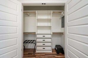 A walk-in closet with open doors, featuring multiple shelves, drawers, and a metal rack.