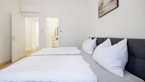 Een slaapkamer met een bed, kussens, een grijs hoofdeinde en een schilderij aan de muur.