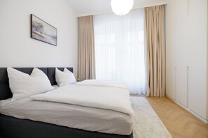 Ein modernes Schlafzimmer mit einem großen Bett, einem Kopfteil, einem Bild an der Wand und einem Fenster mit Vorhängen.