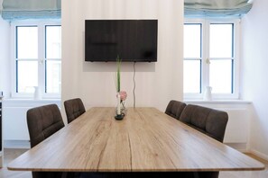 Ein Konferenzraum mit einem großen Holztisch, vier Stühlen, einem an der Wand montierten Flachbildfernseher und großen Fenstern mit blauen Vorhängen.