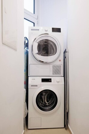 Eine übereinander gestellte Waschmaschine und Trockner in einem Waschraum mit einem Fenster darüber.
