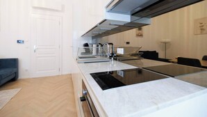 Een moderne keuken met een ingebouwde kookplaat, een magnetron en een afzuigkap. Er is een zithoek met een bank en een eettafel op de achtergrond.
