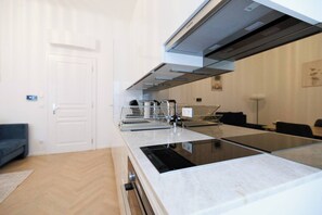 Eine moderne Küche mit Einbauherd, Mikrowelle und Dunstabzugshaube. Im Hintergrund befindet sich eine Sitzecke mit Sofa und Esstisch.
