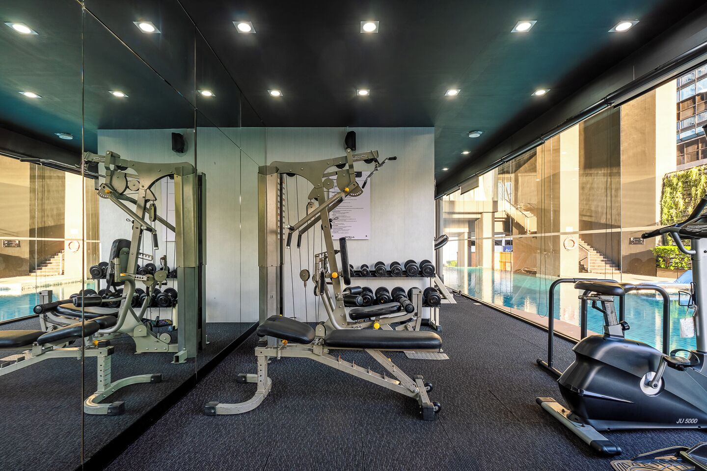 A gym with exercise equipment, a mirrored wall, and a view of a swimming pool.
