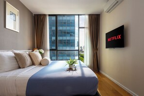 A bedroom with a bed, a TV, a window with curtains, and a plant on the bedside table. - Balcony & Kitchen · Pool, Gym, Fast Wi-Fi (Watthana)