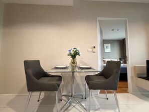 A modern dining area with a glass table, two grey chairs, and a vase with flowers. - Balcony & Kitchen · Pool, Gym, Fast Wi-Fi (Watthana)