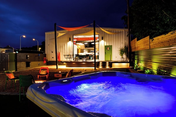 Un bain à remous avec un éclairage bleu, des sièges d’extérieur et un bâtiment doté d’un patio couvert.