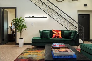 Ein Wohnzimmer mit einem grünen Sofa, einem Couchtisch mit Büchern, einer Treppe und einem Blumentopf.