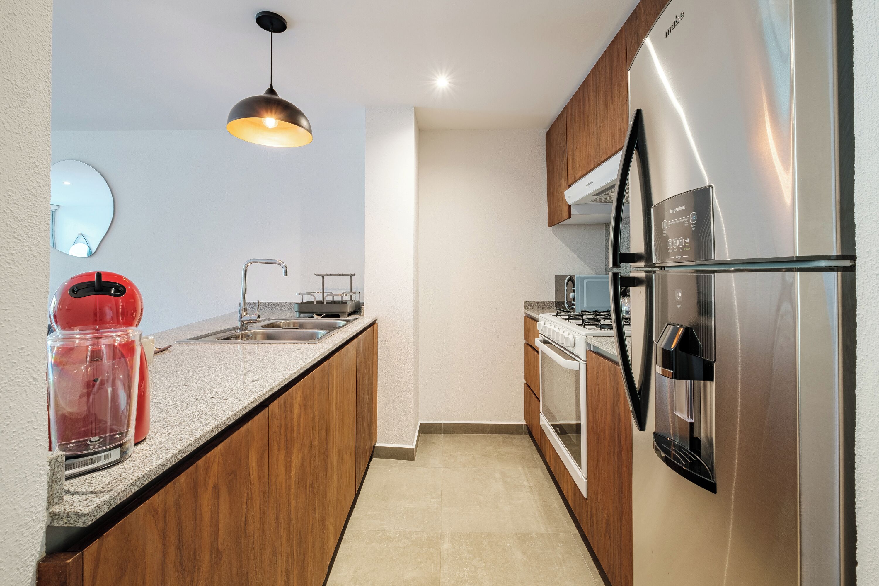 A modern kitchen with a built-in oven, a stainless steel refrigerator, a coffee maker, and a pendant light.
