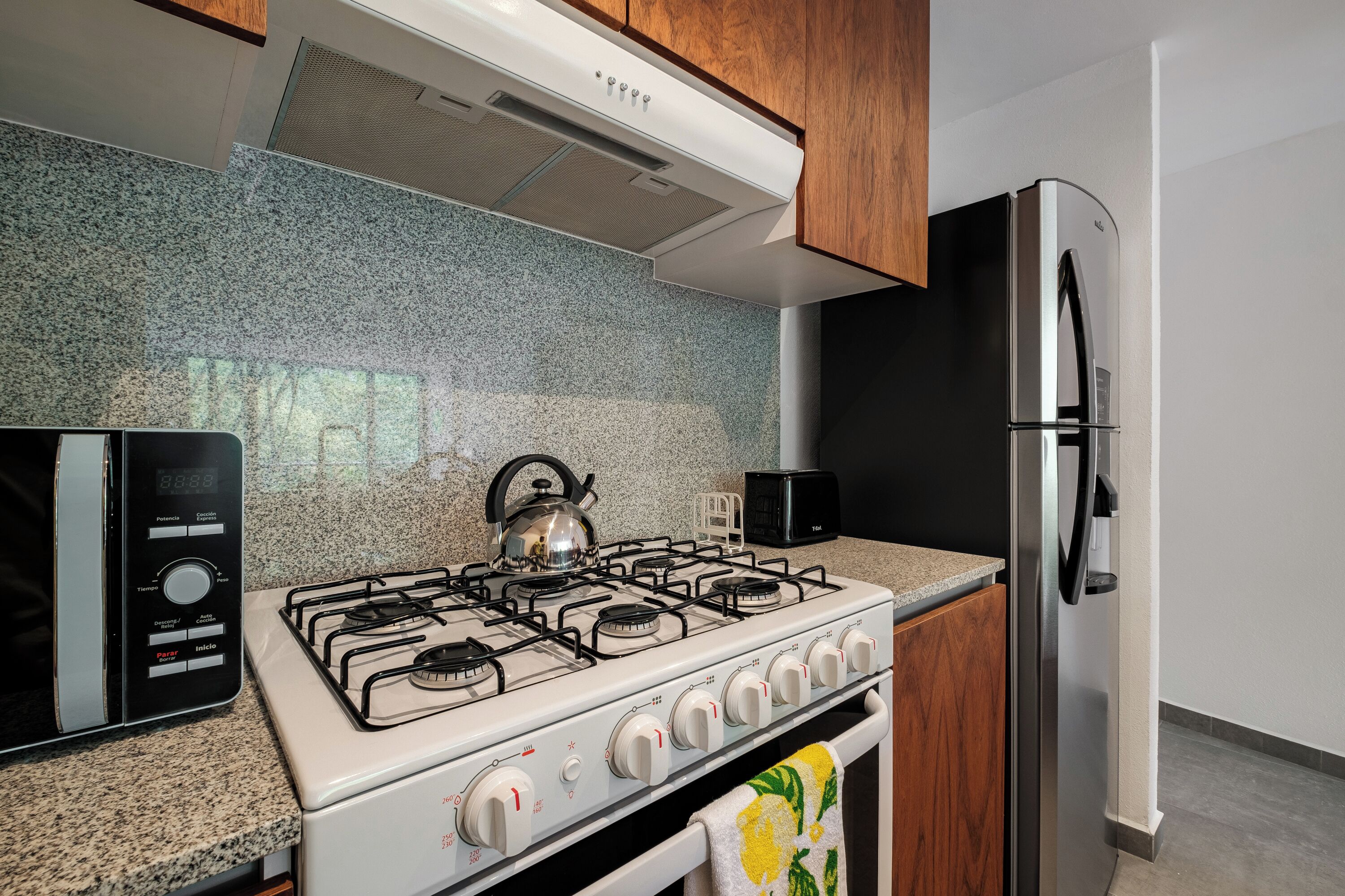 Une cuisine équipée d’une cuisinière à gaz, d’un four à micro-ondes, d’un réfrigérateur et de plans de travail en granit.