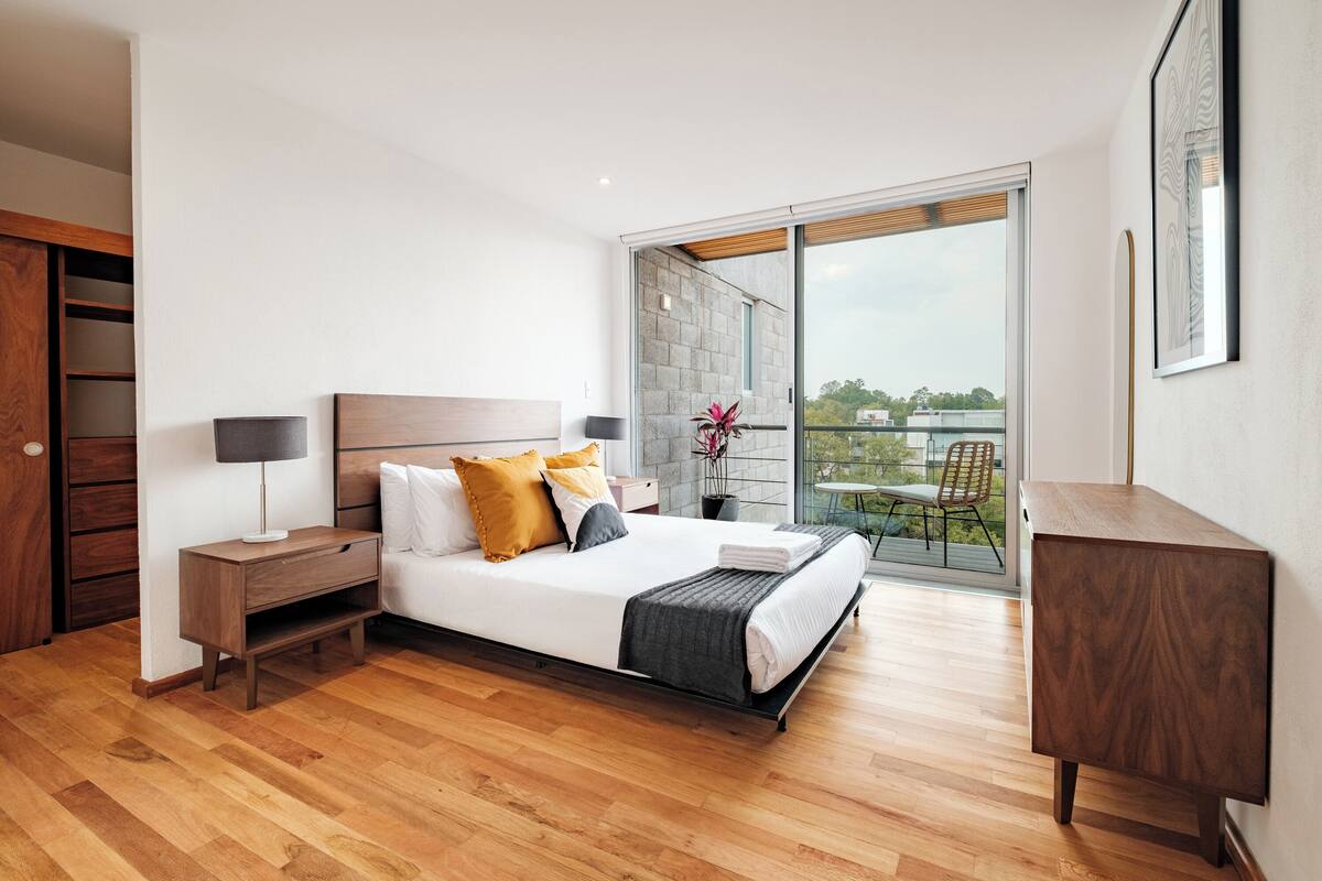 Ein modernes Schlafzimmer mit Bett, Nachttischen, einem Kleiderschrank und einem Balkon mit Blick.
