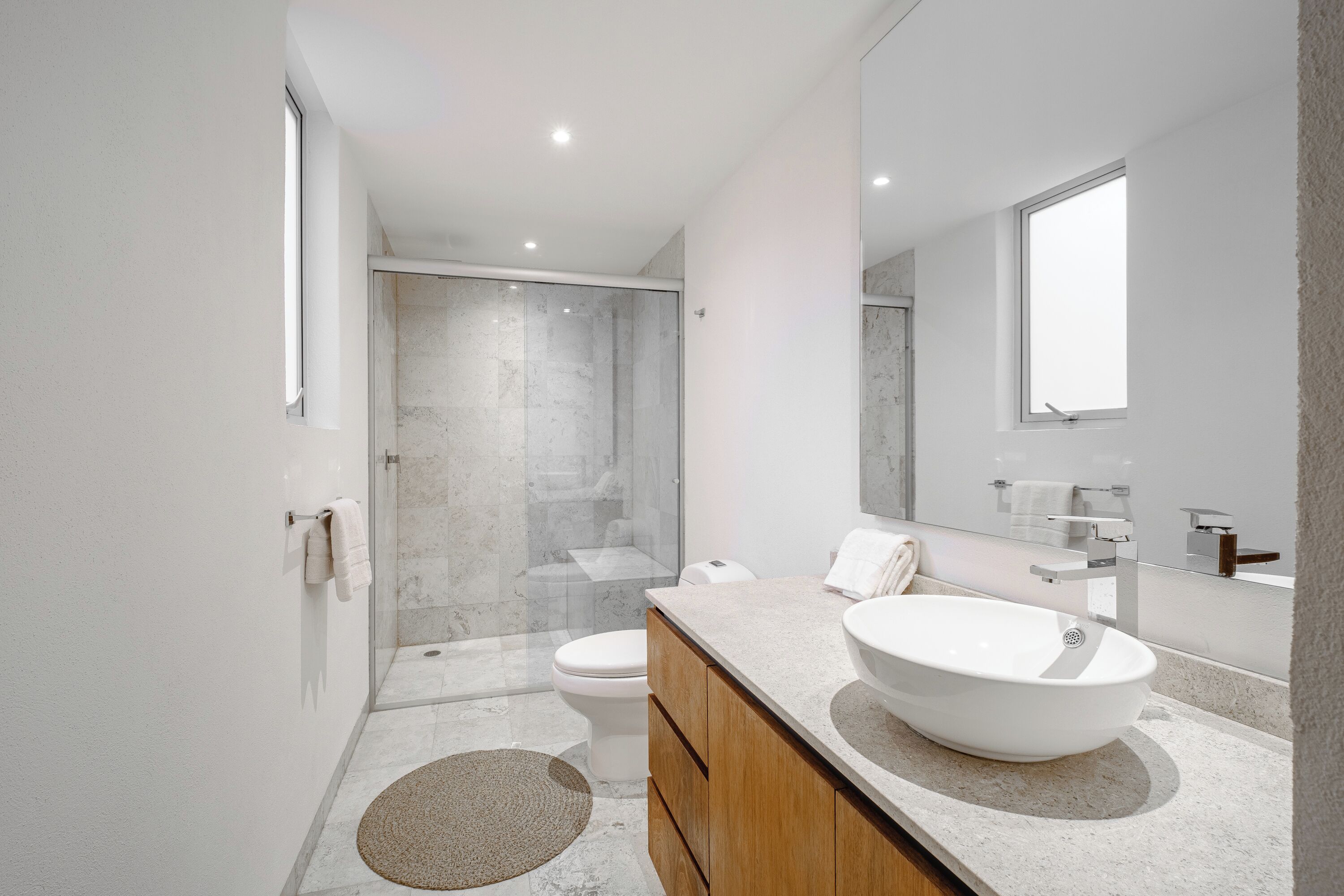 Un baño moderno con un espejo grande, un lavamanos independiente, un inodoro y una cabina de ducha.