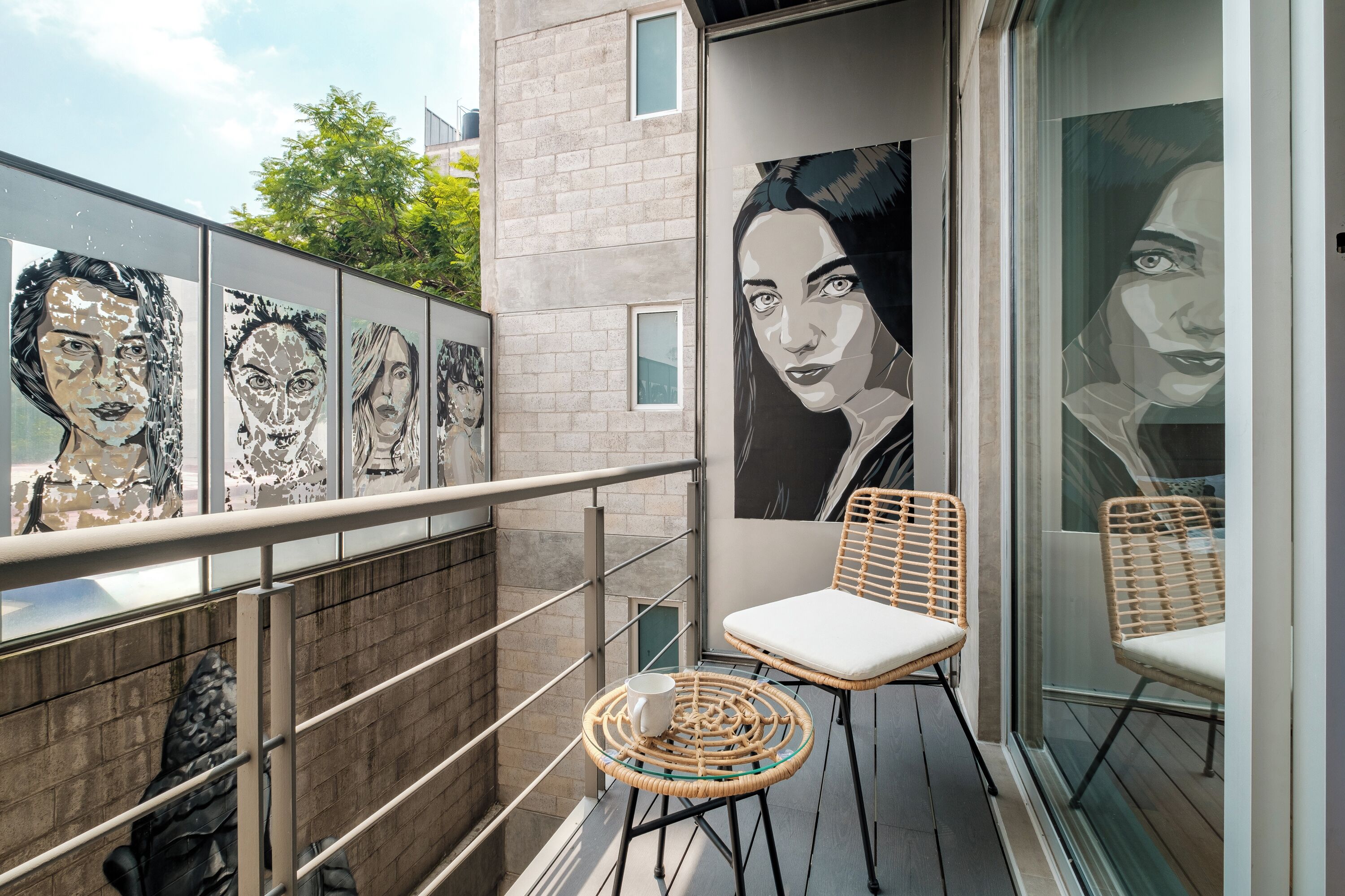 A balcony with a glass railing, wicker chairs, and a large mural on the wall.