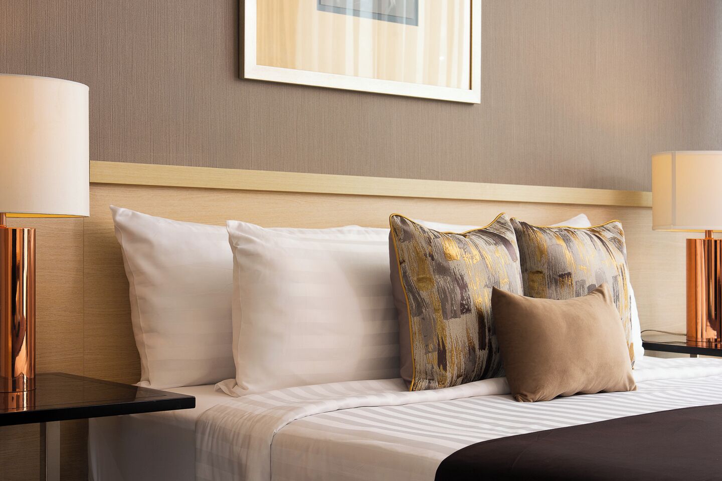 A hotel room with a bed, two bedside lamps, a framed picture on the wall, and a nightstand.