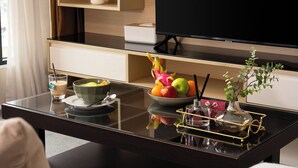 Una habitación de hotel moderna con una mesa de comedor de vidrio, un televisor, una planta en maceta y un frutero.