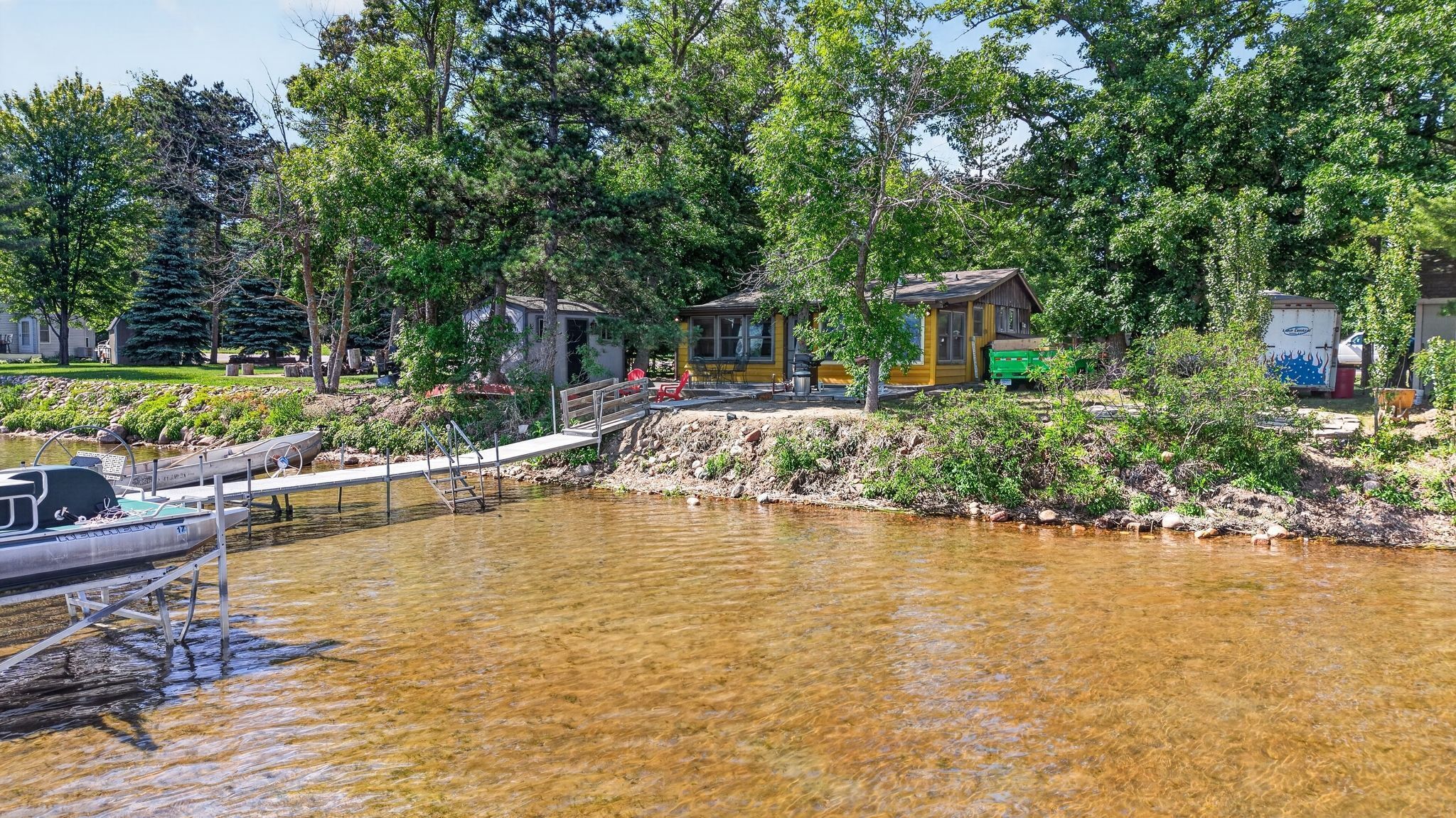 A lakeside cabin with a dock, surrounded by trees and a small boat.
