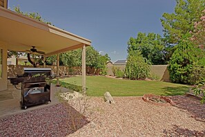 A backyard with a barbecue grill, a covered patio, a well-maintained lawn, and a fire pit area. - Spacious 3-bedroom house in quaint Glendale with AC (Glendale)