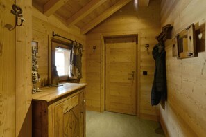 Interior de cabana de madeira com porta de madeira, janela com cortinas, armário de madeira e casaco pendurado na parede.