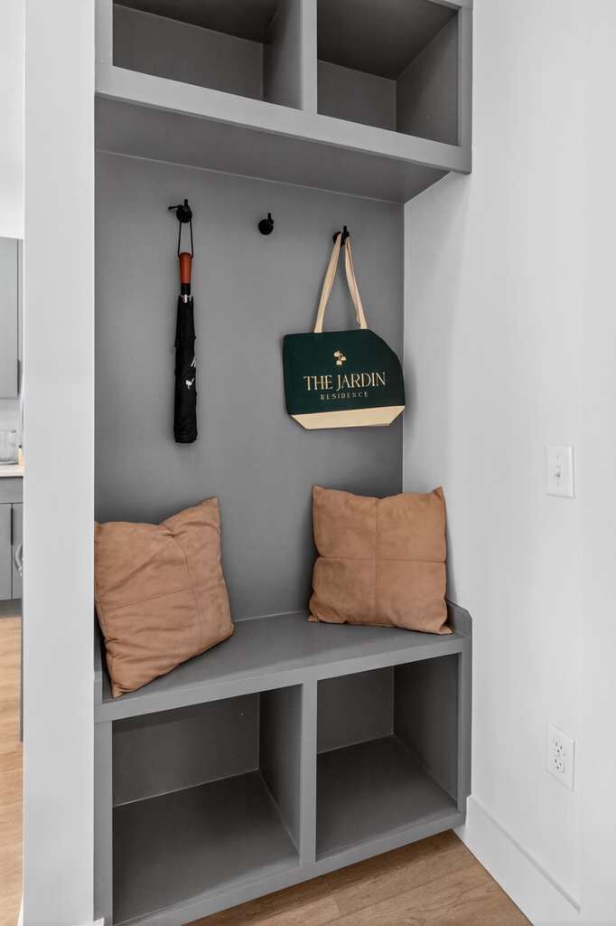 Een grijze bank met twee kussens, een zwarte tas en een groene tas die aan de muur hangt.
