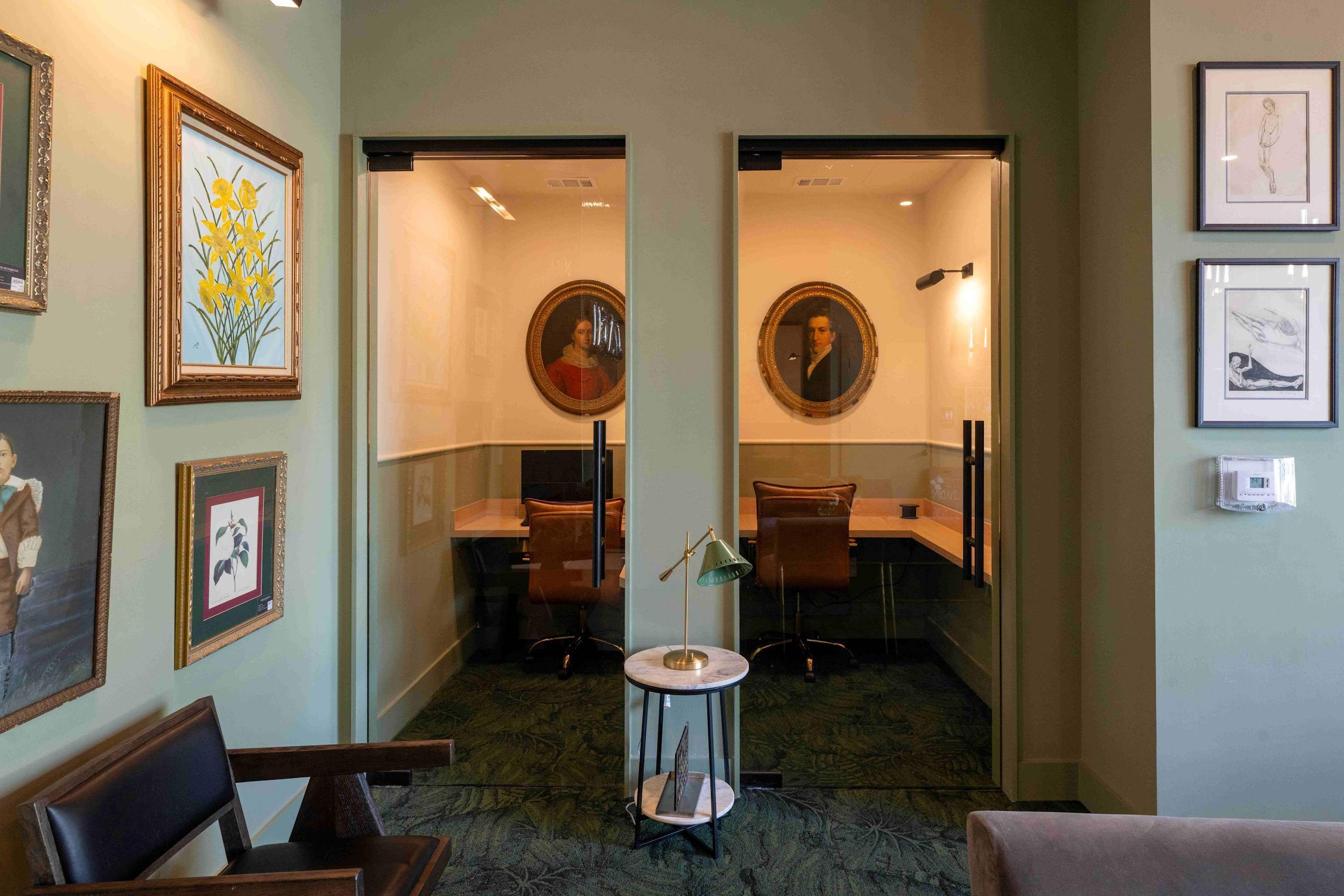 A hallway with framed artwork, a round table with a lamp, and a seating area with chairs.