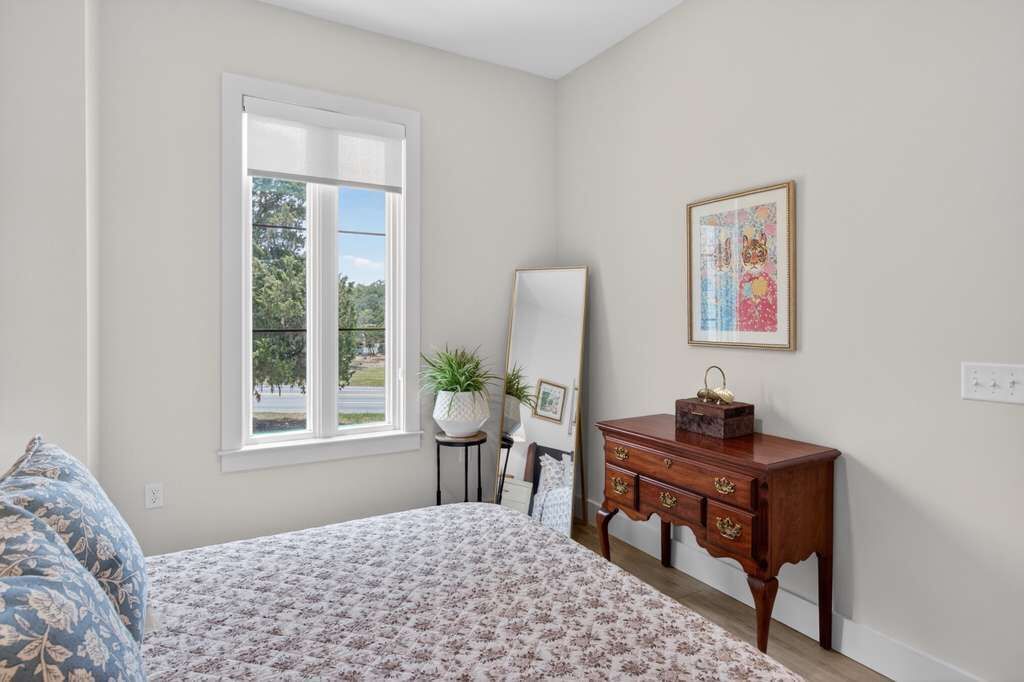 Une chambre à coucher avec un lit, une commode, un miroir et une fenêtre.