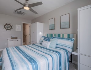 Ein Schlafzimmer mit Bett, Deckenventilator, Kleiderschrank und einer Tür zu einem weiteren Raum.