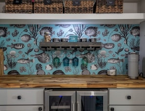 Eine Küche mit Fliesenrückwand mit Meeresmotiven, einer Holz Arbeitsplatte und einem Edelstahl-Kühlschrank.