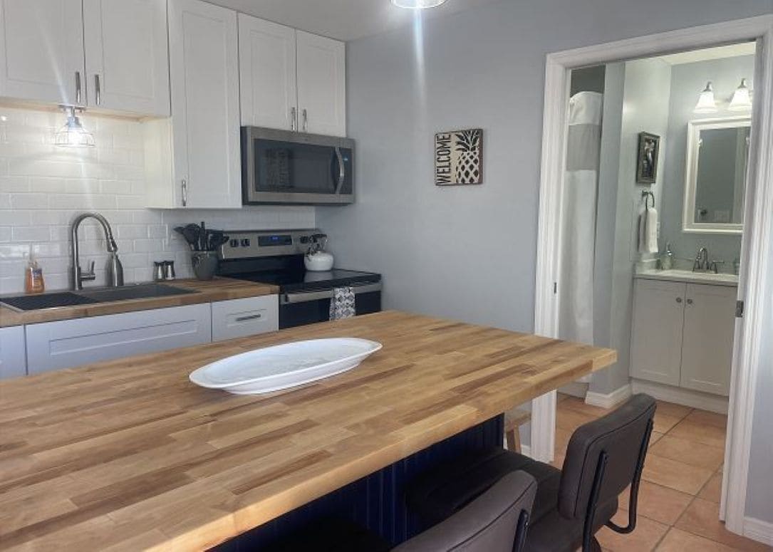 A modern kitchen with white cabinets, a microwave, and a wooden countertop.