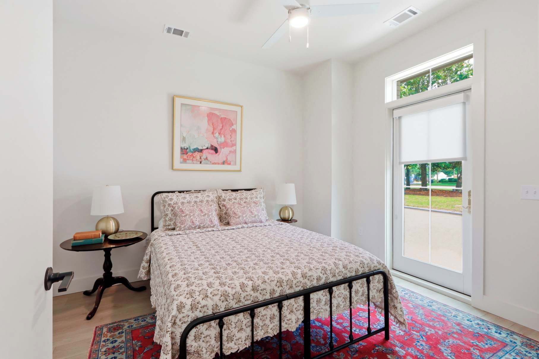 A bedroom with a bed, two bedside tables, a painting, a window, and a door.