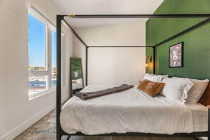 Un dormitorio con cama con dosel, una ventana grande y una pared de acento verde.