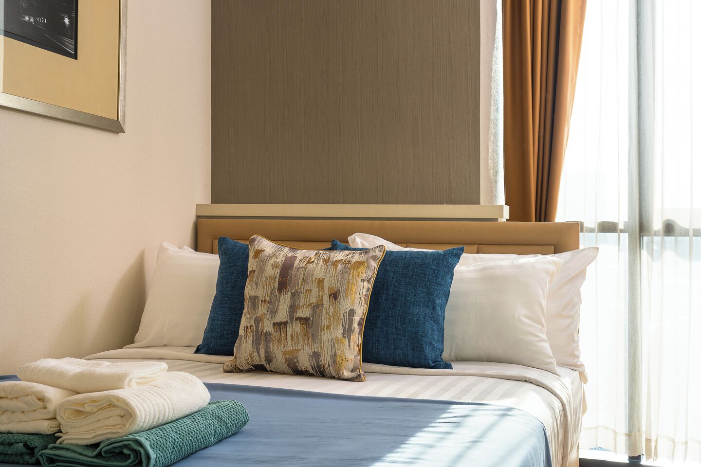 A neatly made bed with a blue bedspread, white pillows, and a decorative pillow.