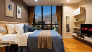 A hotel room with a bed, a TV, a desk, and a large window with a city view. - Skyline View · Pool, Gym, Fast Wi-Fi (Watthana)