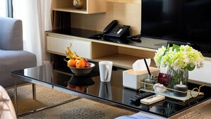 A modern hotel room with a glass coffee table, a bowl of fruit, a vase of flowers, a remote control, and a telephone. - Skyline View · Pool, Gym, Fast Wi-Fi (Watthana)