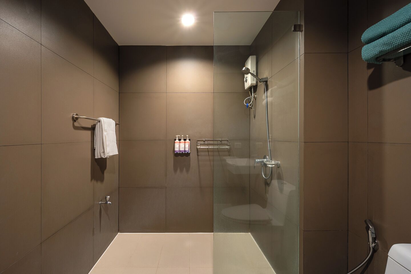 A modern bathroom with a glass-enclosed shower, a towel rack, and a shelf with toiletries.