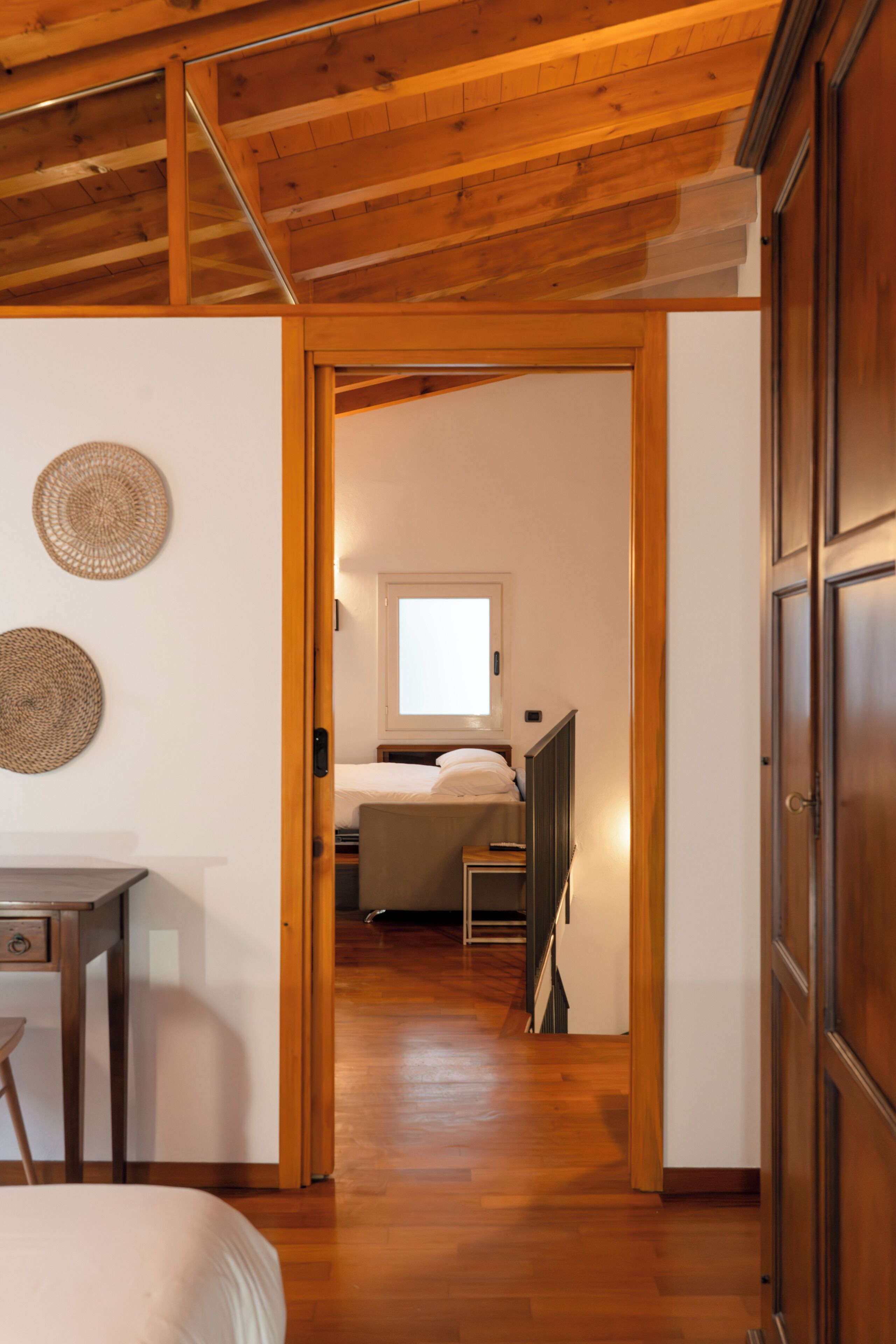 A hallway leading to a bedroom with a bed, a desk, and a wardrobe.
