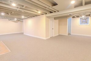 Une pièce spacieuse et vide, aux murs blancs, recouverte d’un tapis beige et dont les poutres apparentes du plafond sont visibles.