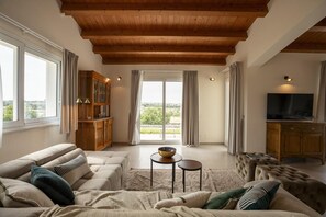 Ein Wohnzimmer mit Holzboden, einer Sofagarnitur, einem Fernseher und Blick durch eine Glastür.