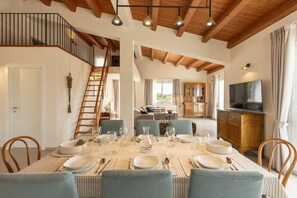 Ein Essbereich mit einem für sechs Personen gedeckten Tisch, eine Treppe, ein Wohnzimmer und ein Fernseher im Hintergrund.