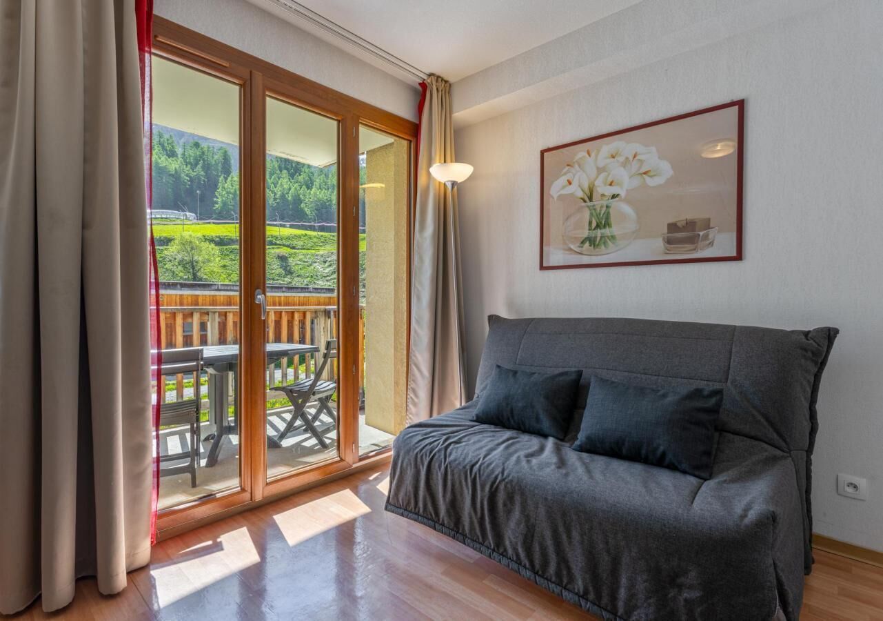 Ein Zimmer mit einer Couch, einer Schiebetür zu einem Außenbereich mit Tisch und Stühlen sowie einem gerahmten Bild an der Wand.