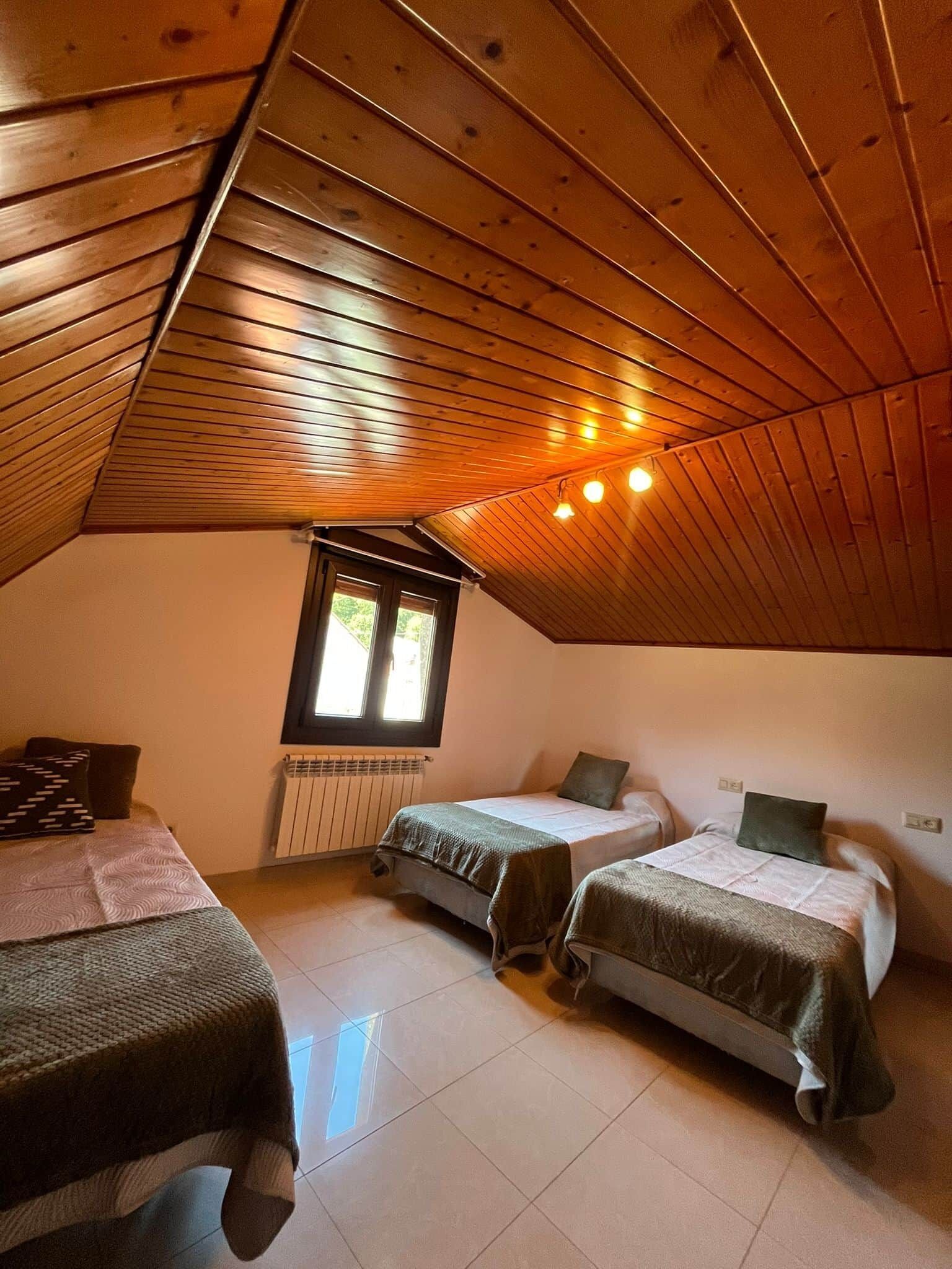 Een gezellig slaapkamer op zolder met houten schuine plafonds, twee eenpersoonsbedden, een raam en een radiator.
